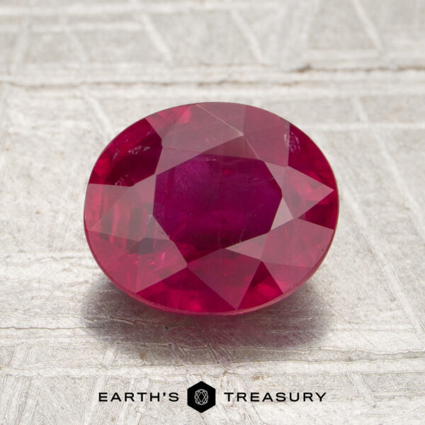 2.07-Carat Mozambique Ruby (Heated) A 2.07-carat Mozambique ruby (heated), cut in an oval shape, is displayed on a light gray textured surface with “Earth’s Treasury” text below.