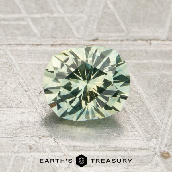 1.27-Carat Mint Green Montana Sapphire (Heated) A 1.27-carat mint green Montana sapphire (heated) rests on a textured surface, with the words “EARTH’S TREASURY” and a hexagon logo displayed below it.