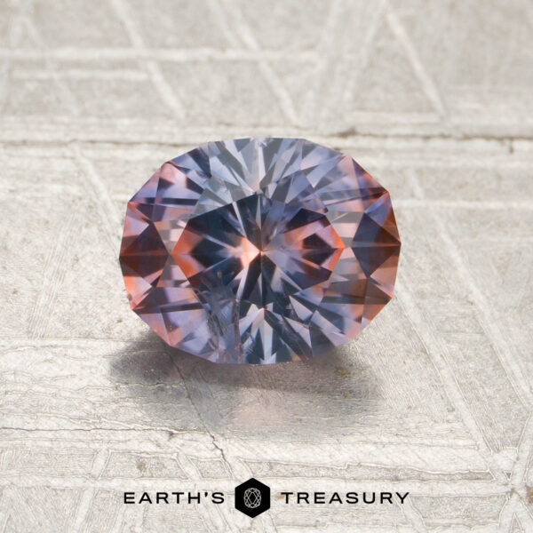 1.61-Carat Purple-Orange Particolored Montana Sapphire (Heated) A 1.61-carat purple-orange particolored Montana sapphire (heated) with striking blue and orange hues rests on a textured metallic surface, while the “EARTH’S TREASURY” logo and text appear at the bottom.