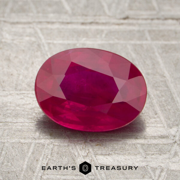 1.97-Carat Burmese Ruby (Heated) A 1.97-carat Burmese ruby (heated), cut in an oval faceted shape, is displayed on a textured gray surface. The text “EARTH’S TREASURY” appears at the bottom of the image.