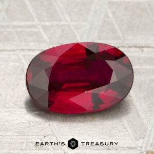 A 2.01-carat heated Mozambique ruby in an oval cut is displayed on a textured surface, with “Earth’s Treasury” appearing at the bottom of the image.