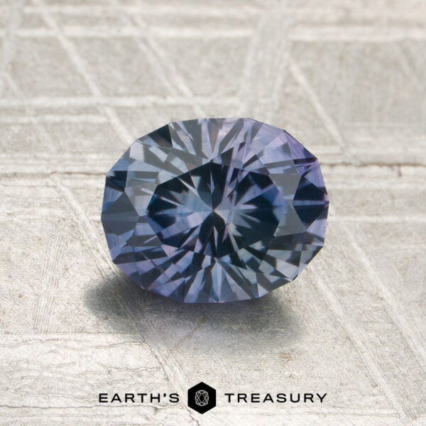 1.53-Carat Steely Violet Montana Sapphire (Heated) A 1.53-carat steely violet Montana sapphire (heated), oval-cut, is displayed on a textured metallic surface featuring the “Earth’s Treasury” name and logo below.