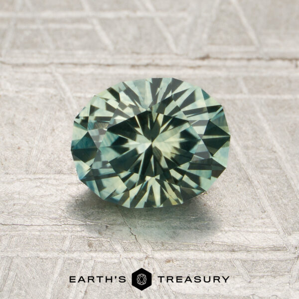 1.52-Carat Rich Mint Green Montana Sapphire (Heated) A 1.52-carat rich mint green Montana sapphire (heated) rests on a textured metallic surface, with the text “Earth’s Treasury” below the stone.