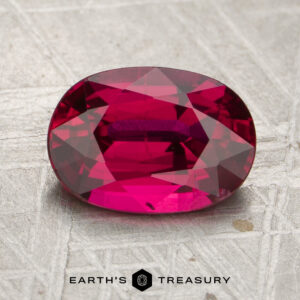 2.25-Carat Mozambique Ruby (Heated), oval-cut and deep pink, displayed on a textured surface, with the “EARTH’S TREASURY” logo and text at the bottom.