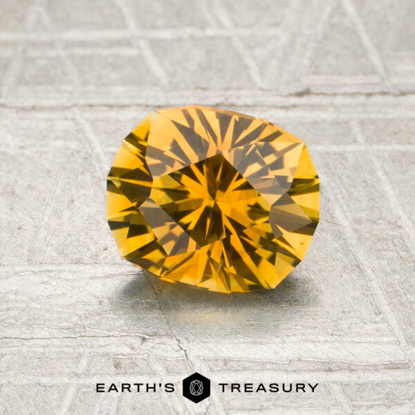 1.16-Carat Rich Golden Yellow Montana Sapphire (Heated) A 1.16-carat rich golden yellow Montana sapphire (heated) is displayed on a textured gray surface with the words “EARTH’S TREASURY” at the bottom.