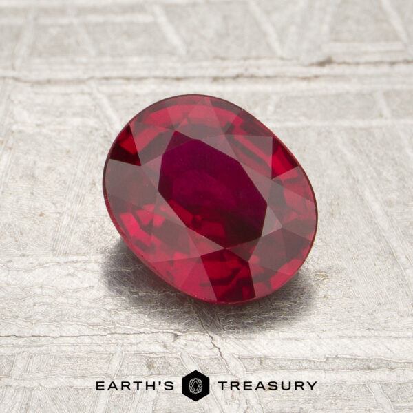 A 1.20-carat, oval-shaped faceted Mozambique ruby (heated) rests on a textured light surface, with the words “Earth’s Treasury” displayed at the bottom of the image.