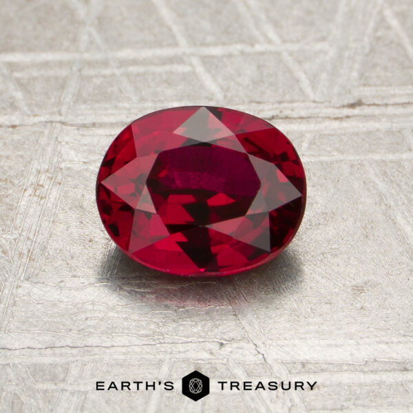 A 1.20-carat heated Mozambique ruby, expertly cut in an oval shape, is displayed on a textured surface. The “EARTH’S TREASURY” logo is visible at the bottom of the image.