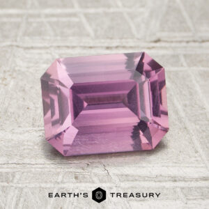 A 2.08-carat pink sapphire, cut in a rectangular faceted shape, is displayed on a textured light surface with the text “EARTH’S TREASURY” at the bottom.