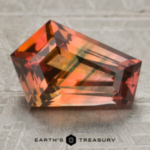 A 4.00-carat orange-blue particolored sapphire (heated) rests on a textured surface, with the “Earth’s Treasury” logo visible at the bottom of the image.