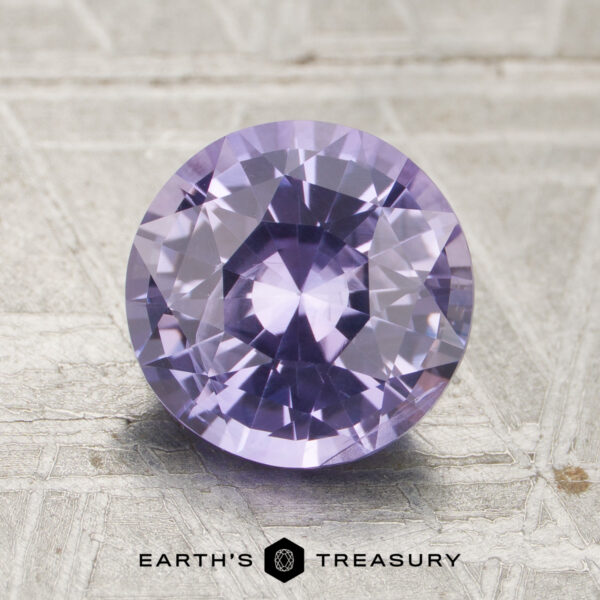 2.02-Carat Lavender Ceylon Sapphire (Heated) A 2.02-carat, round-cut, faceted lavender sapphire (heated) is displayed on a textured surface with the text “Earth’s Treasury” below.