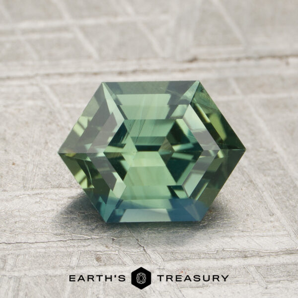 1.61-Carat Green Madagascar Sapphire (Heated) A 1.61-carat green Madagascar sapphire (heated) with hexagonal geometric facets is displayed on a textured surface, with the “EARTH’S TREASURY” logo beneath the stone.