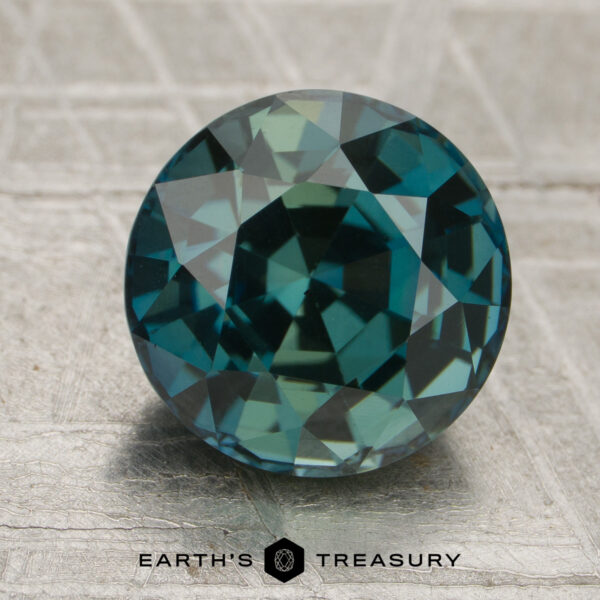 3.52-Carat Deep Teal Madagascar Sapphire (Heated) A 3.52-carat deep teal Madagascar sapphire (heated) is showcased on a textured surface, with the words “Earth’s Treasury” and a hexagonal logo visible at the bottom of the image.