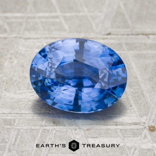 3.55-Carat Rich Cornflower Blue Ceylon Sapphire (Heated) A 3.55-carat cornflower blue to violet color-change Ceylon sapphire, oval-shaped, displayed on a textured gray surface with the “EARTH’S TREASURY” logo and text beneath it.
