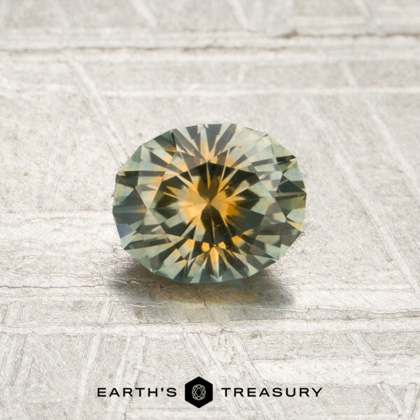 0.85-Carat Mint Green-Orange Particolored Montana Sapphire (Heated) A 0.85-carat mint green-orange particolored Montana sapphire (heated) is displayed on a textured surface with the text “EARTH’S TREASURY” at the bottom.