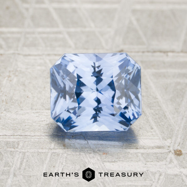 3.14-Carat Sky Blue Ceylon Sapphire (Heated) A 3.14-carat sky blue to pale violet color-change Ceylon sapphire with a rectangular faceted cut is placed on a textured light surface, with the “EARTH’S TREASURY” logo and text visible below.