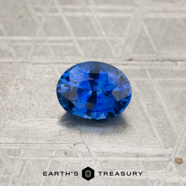 1.19-Carat Rich Blue Ceylon Sapphire (Heated) A 1.19-carat rich blue to violet color-change Ceylon sapphire is displayed on a textured, metallic surface, with “EARTH’S TREASURY” appearing at the bottom.