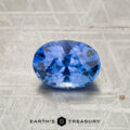 A 2.23-carat Cornflower Blue to Violet color-change Ceylon sapphire, expertly cut in an oval shape, rests on a textured gray surface with the Earth’s Treasury logo at the bottom.