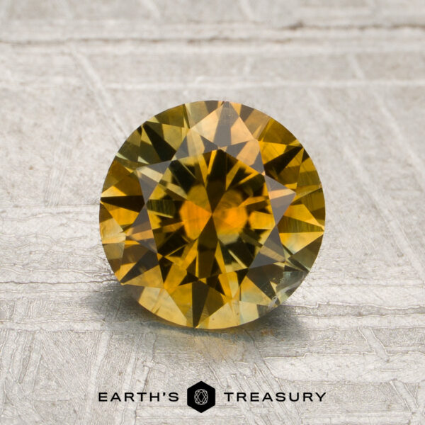 1.56-Carat Golden Yellow Montana Sapphire (Heated) A round, faceted 1.56-carat golden yellow Montana sapphire (heated) is displayed on a textured, light-colored surface with the text “Earth’s Treasury” below.