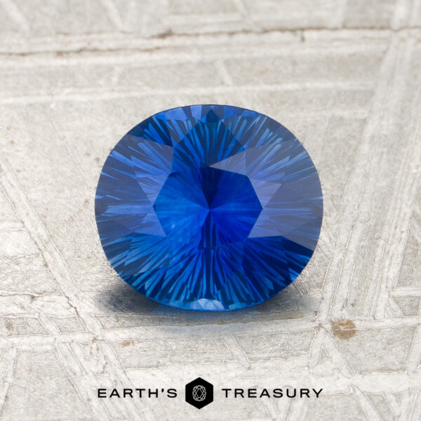 1.18-Carat Royal Blue Ceylon Sapphire (Heated) 1.18-carat royal blue Ceylon sapphire (heated), oval-cut, showcased on a textured surface with the “Earth’s Treasury” logo and text at the bottom of the image.