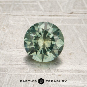 1.09-carat mint green Montana sapphire (heated) with a faceted cut, displayed on a textured light surface above the text “EARTH’S TREASURY.”.