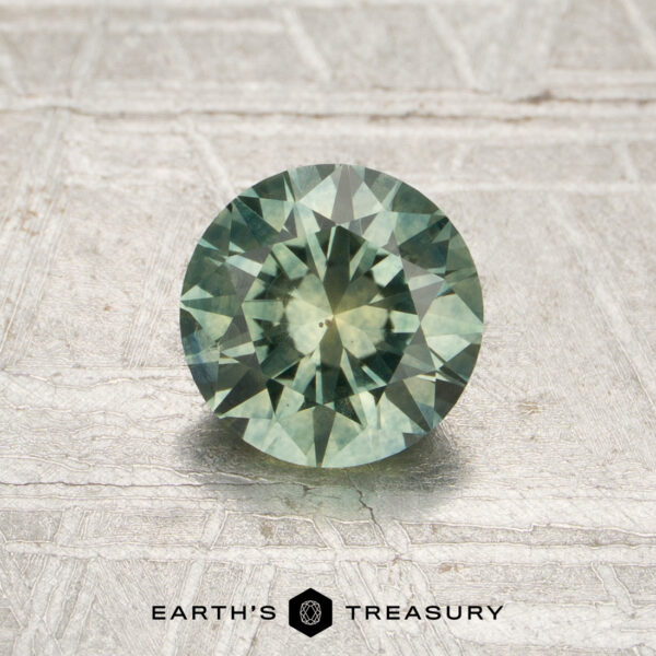 1.09-Carat Mint Green Montana Sapphire (Heated) 1.09-carat mint green Montana sapphire (heated) with a faceted cut, displayed on a textured light surface above the text “EARTH’S TREASURY.”.