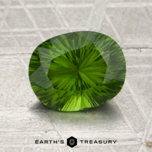 A 1.78-carat oval-cut Kenya tourmaline with intricate faceting rests on a textured gray surface, with the Earth’s Treasury logo visible at the bottom.