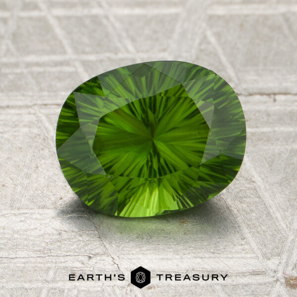 A 1.78-carat oval-cut Kenya tourmaline with intricate faceting rests on a textured gray surface, with the Earth’s Treasury logo visible at the bottom.