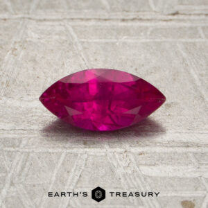 A 0.61-carat marquise ruby (heated) is displayed on a textured gray surface, with the “EARTH’S TREASURY” logo and text at the bottom of the image.