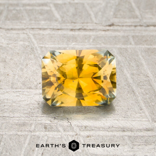 0.98-Carat Golden Yellow Montana Sapphire (Heated) A radiant-cut, rectangular golden yellow Montana sapphire (0.98 carats, heated) is displayed on a textured gray surface, with the “Earth’s Treasury” logo and text at the bottom of the image.
