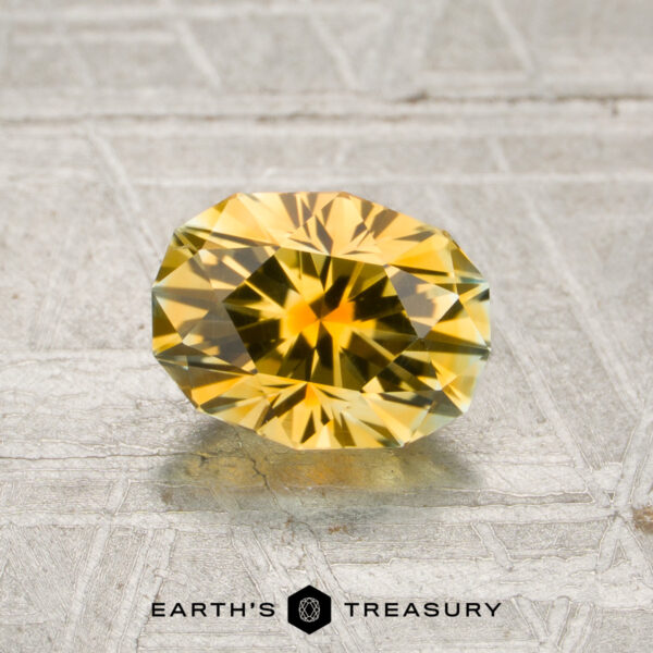 1.40-Carat Golden Yellow Montana Sapphire (Heated) A 1.40-carat golden yellow Montana sapphire (heated) rests on a textured gray surface with the words “Earth’s Treasury” below.