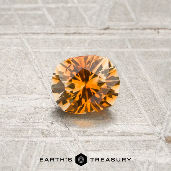 0.70-Carat Orange-Pale Yellow Particolored Montana Sapphire (Heated) A 0.70-carat orange-pale yellow particolored Montana sapphire rests on a textured silvery surface, with “EARTH’S TREASURY” displayed below.