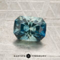 A 1.74-carat aqua-blue particolored Montana sapphire (heated), cut in a rectangular faceted shape, is displayed on a textured gray surface with the “Earth’s Treasury” logo below.