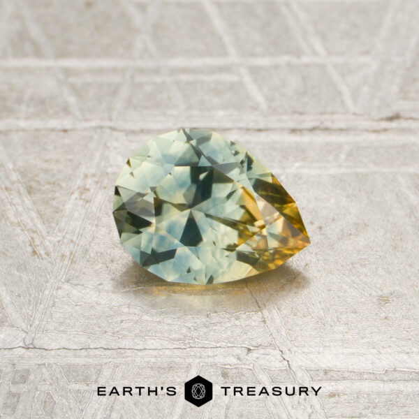 0.82-Carat Aqua-Yellow Particolored Montana Sapphire (Heated) A faceted pear-shaped 0.82-carat aqua-yellow particolored Montana sapphire (heated) with green and yellow hues rests on a textured surface above the text “Earth’s Treasury.”.