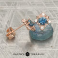 The "Marisol" Stud Earrings in 14K Rose Gold featuring blue gemstones and small white diamonds displayed on a blue crystal, with the text “Earth’s Treasury” at the bottom.