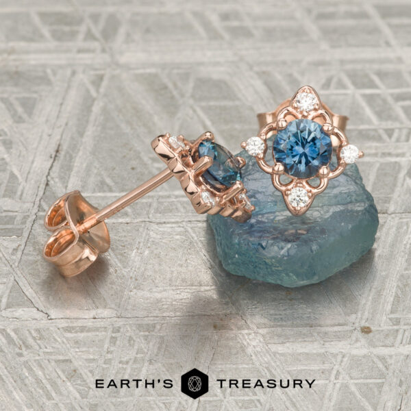 The "Marisol" Stud Earrings in 14K Rose Gold The "Marisol" Stud Earrings in 14K Rose Gold featuring blue gemstones and small white diamonds displayed on a blue crystal, with the text “Earth’s Treasury” at the bottom.